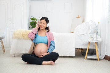 Pregnant woman sitting on floor in cozy modern home, listening to music with headphones, gently touching belly, maternity bonding, emotional wellness, prenatal care, lifestyle, motherhood, relaxation