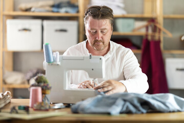 Man seamstress operating by sewing machine, manufactures clothing