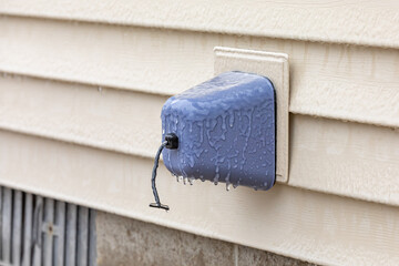 Outdoor faucet, water spigot, with ice on insulation cover. Home maintenance, winter weather preparation and winterize plumbing concept.
