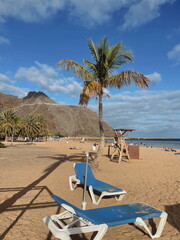 Sun loungers under a palm tree on a tropical beach with golden sand. Perfect vacation scene, peaceful and relaxing coastal atmosphere.