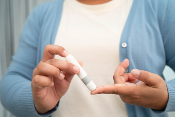 Asian woman self testing to check blood sugar level diabetes by digital lancet on finger at home.
