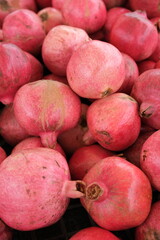 A vibrant pile of pinkish-red pomegranates fills black crates, each fruit varying slightly in hue and size.