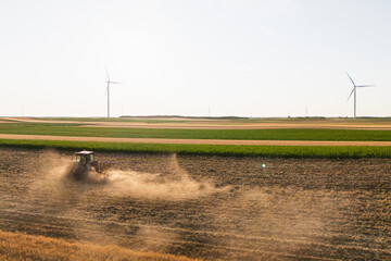 Agricultural tractor is working on the field with wind turbines. Aerial view
