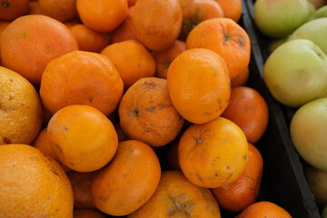 The image shows a close-up pile of oranges and tangerines in various shades of orange. Some fruits display minor blemishes or spots, adding to the natural, unprocessed look.