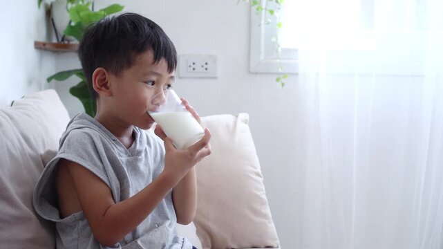 Asian boy smiling while drinking a glass of fresh milk at home, enjoying the tasty and nutritious drink rich in calcium. Promoting a healthy lifestyle, strong bones, and a balanced diet for growing 