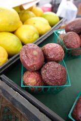 The image shows a collection of passion fruits arranged on a black plastic crate with a grid pattern. The fruits vary in appearance&mdash;some are wrinkled and brownish