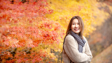 A young woman enjoys the colorful autumn leaves, wrapped in cozy clothes and a scarf. Perfect for themes like fall, travel fashion or happiness.
