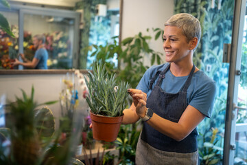 Smiling young female florist nurturing potted plants in her small flower shop, proud of her thriving business