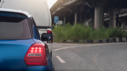 Rear side of mini car blue color with turn on brake light. Parking behind a cargo car. Side of car with curved asphalt road for U-Turn under level bridge.