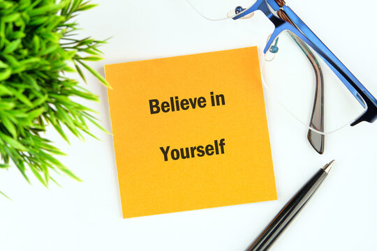A bright orange note displays the words Believe in Yourself next to blue Glasses and a Pen, near a green plant. It suggests self-motivation and focusing on Goals