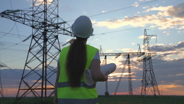 An electrician on the background of high towers of power plants looks at the project for the development of an electrical structure, the expansion of the electrical voltage of volts in the wires.