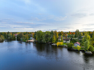 Obraz premium Aerial view of a village with small houses nestled among trees with colorful autumn foliage along the edge of a wide river