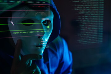 male hacker wearing a white mask sits in front of a screen, hands typing amid glowing cyber attack alerts and red binary code, symbolizing hacking, data breach, and malware concepts.