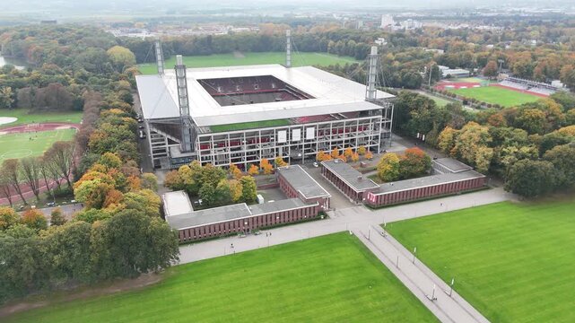 Cologne, Germany - 12 October, 2025: aerial view of a modern Muengersdorf football stadium aligned with a central walkway and lawns, set within a forested urban park. No people. Symmetry