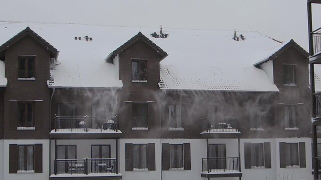 wind blows snow off the roofs during a snowfall