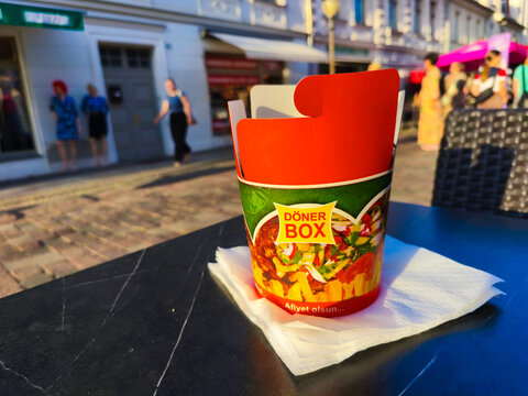 Potsdam, Germany - September 20, 2025: Colorful Doner Box filled with delicious ingredients sits on a table in a vibrant street scene, showcasing urban dining culture and culinary delight