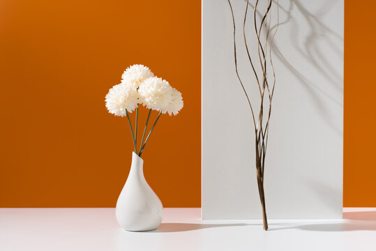 Flores de crisantemo blancas decorativas en un jarr&oacute;n blanco sobre fondo naranja	
