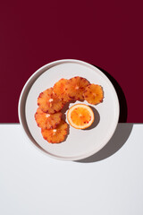 Rodajas de naranja sanguina peladas sobre un plato blanco con fondo blanco y granate. Vista superior