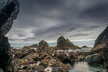 Moody Irish shoreline seen through a rock arch, with wet boulders and stormy ocean beyond.