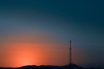 Naklejka premium Colorful sunset sky sun setting behind mountains in deserted terrain mobile communication tower