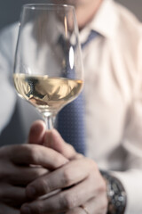 Torso of man in white shirt with open collar and loose tie and glass of white wine