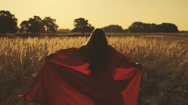 happy girl play superheroes they run across green field in red cloak, cloak flutters in wind. children's games and dreams. Slow motion. teenager dreams of becoming superhero. young girls in red cloak. - Powered by Adobe