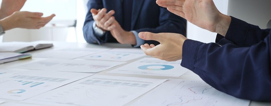 Teamwork and business collaboration with colleagues joining hands over financial charts, symbolizing unity, partnership, success, and strategic corporate planning