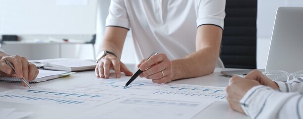 Professional business team reviewing financial data, collaborating over charts and graphs with laptop and pen in contemporary workplace, emphasizing strategic analysis and teamwork