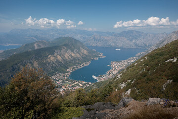 Obraz premium Kotor bay azure water surrounded by rocky mountains and towns along shore on sunny day, Montenegro