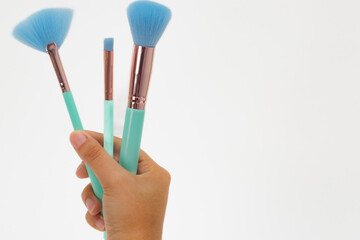 A hand holding three green and blue makeup brushes. The brushes are of different sizes and are held together in a bundle