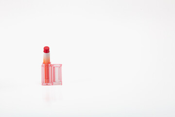 A small red lipstick is sitting on a white background. The lipstick is the main focus of the image, and it is a close-up shot. The white background emphasizes the lipstick's color.