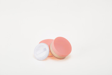 A pink container with a white lid sits on a white background. The container is likely a makeup product, such as a blush or eyeshadow. The pink color of the container.
