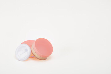A pink container with a white lid sits on a white background. The container is a makeup compact and is placed on top of another container. Concept of organization and cleanliness.