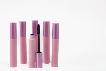 A row of six pink mascara tubes with a black brush in the middle. Concept of organization and order, as the tubes are neatly lined up.