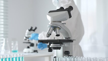 Modern microscopes and test tubes containing blue liquid are arranged on a table in a bright...