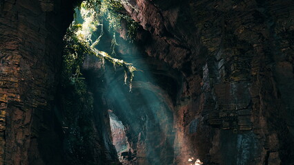 Sunlight streams into a dark cave, highlighting vibrant green plants clinging to the rocks. Shadows dance as beams of light create an enchanting atmosphere, inviting exploration and wonder.