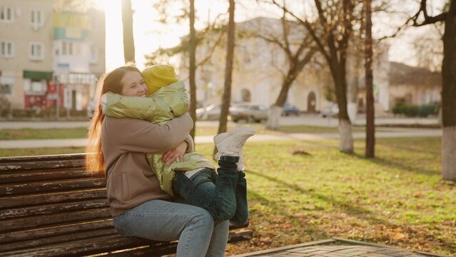 happy mom hugs little child son park sunset. warm autumn day. child kid runs hug mother. maternal care love. teamwork outdoors. good mood woman. children holidays. happy family walk. smiling mom - Powered by Adobe
