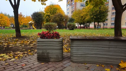 Urban park with benches and flower pots made from concrete using a 3D printer surrounded by autumn foliage  