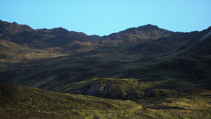 Rolling hills stretch across the landscape, covered in vibrant green grass and illuminated by the warm hues of twilight. The mountains form a dramatic backdrop against the serene sky.