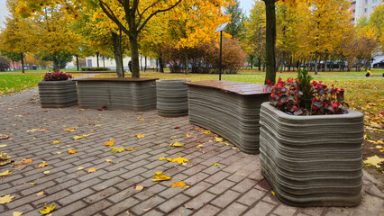 Modern concrete benches with flowers pots made from concrete using a 3D printer in autumn park setting  