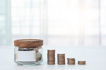 Jar with money inside with empty label and stacked coins with blurred background. Finance business concept.