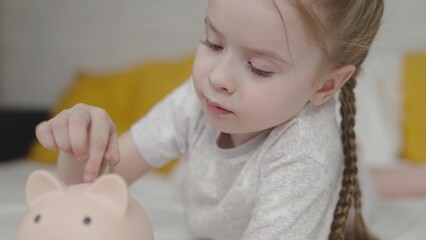 happy little girl throws coins into piggy bank, kid learns count his finances, an interesting baby game, child saves up for dream life, love money from childhood, to be able to save up for purchases.