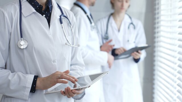 Medical professional using a digital tablet for patient care and data management, collaborating with doctors and healthcare workers in a modern clinic or hospital setting