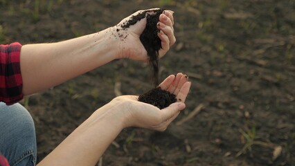 A woman farmer pours plowed land from one hand to another, preparing the fields for planting vegetables and fruit trees.