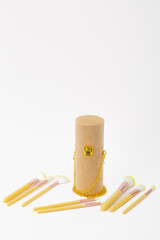 A set of makeup brushes are displayed in a wooden case. The case is gold and has a chain hanging from it. The brushes are of different sizes and colors, and they are arranged in a row