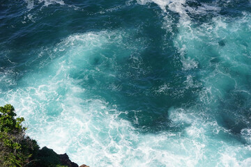 Waves crashing against a cluster of dark brown rocks. The water is a stunning mix of deep blue and...