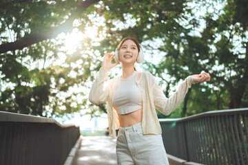 Happy young Asian woman listening to music with wireless headphones outdoors, smiling girl enjoying...