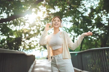 Fotobehang Beren Happy young Asian woman listening to music with wireless headphones outdoors, smiling girl enjoying sunshine and relaxing walk on bridge in city park, lifestyle freedom and wellness concept in summer   © oatawa
