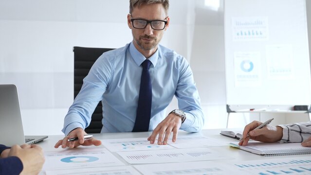 Business professional presenting financial strategy during corporate meeting with colleagues, analyzing charts and discussing data for growth and success planning