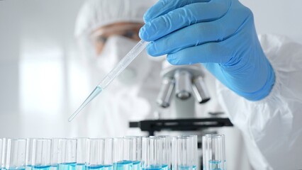 Scientific researcher wearing protective equipment, carefully pipetting liquid into test tubes...